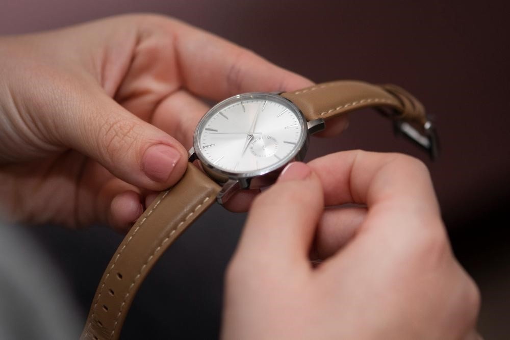 man winding classic white dial watch with brown leather band